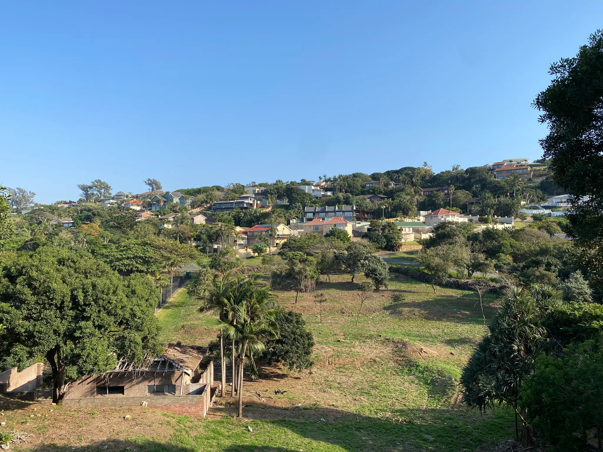 Houses nestled on a lush, green hillside against a blue sky in Zinkwazi.