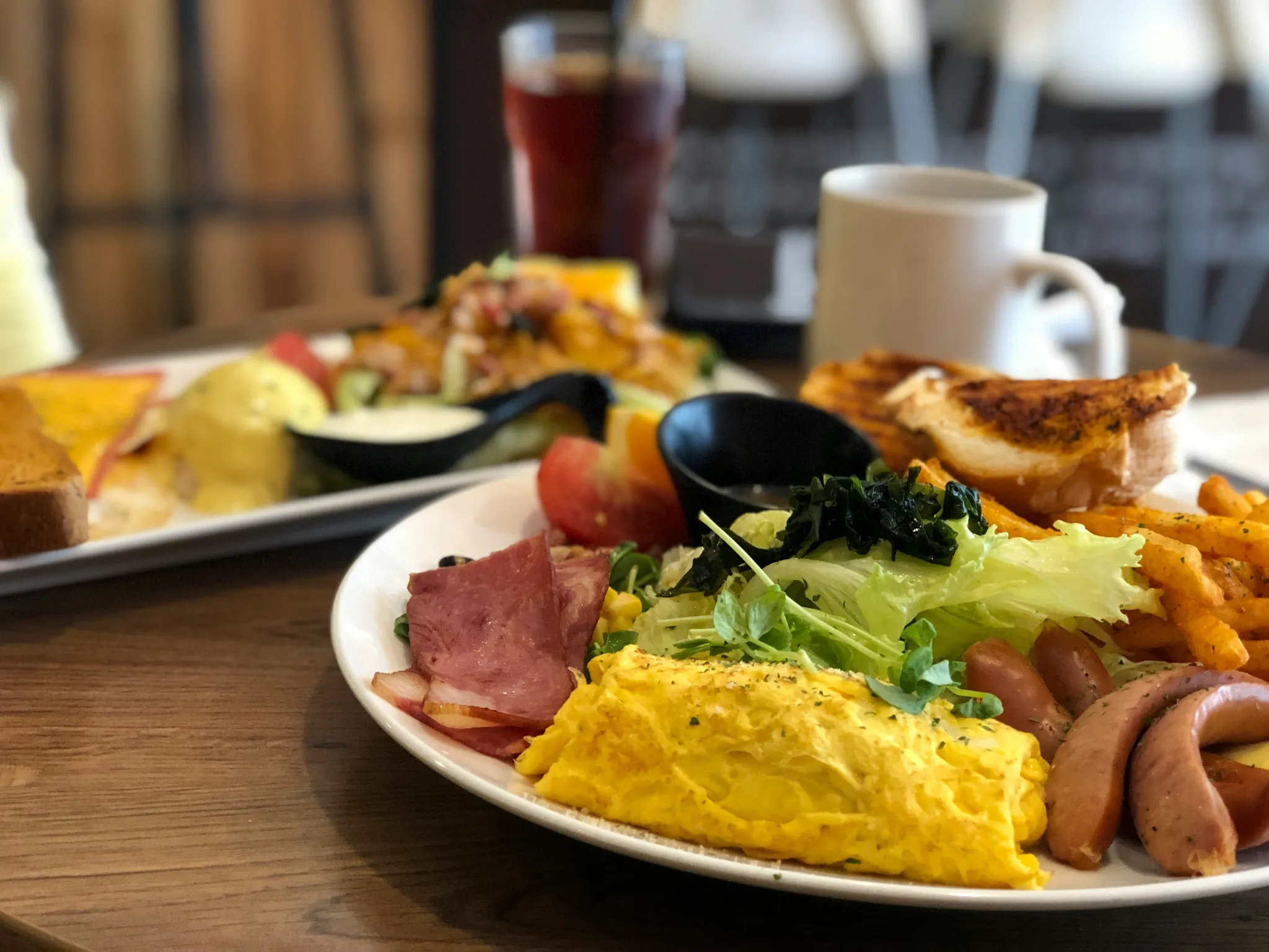 A full breakfast plate with omelette, sausages, bacon, salad, and fries at a Ballito restaurant.