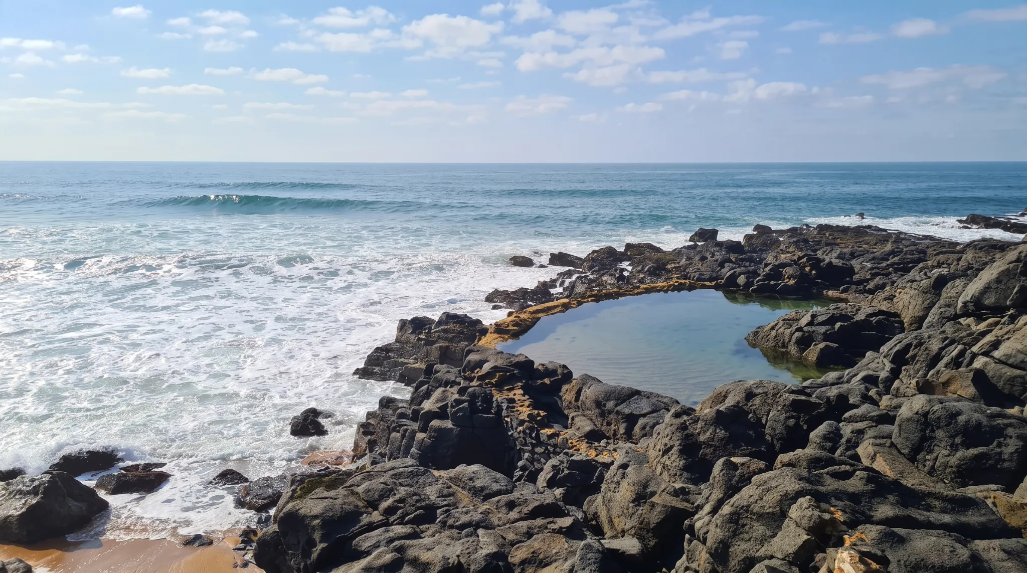 A protected tidal pool among rocks and foamy waves on a sunny day in Ballito.
