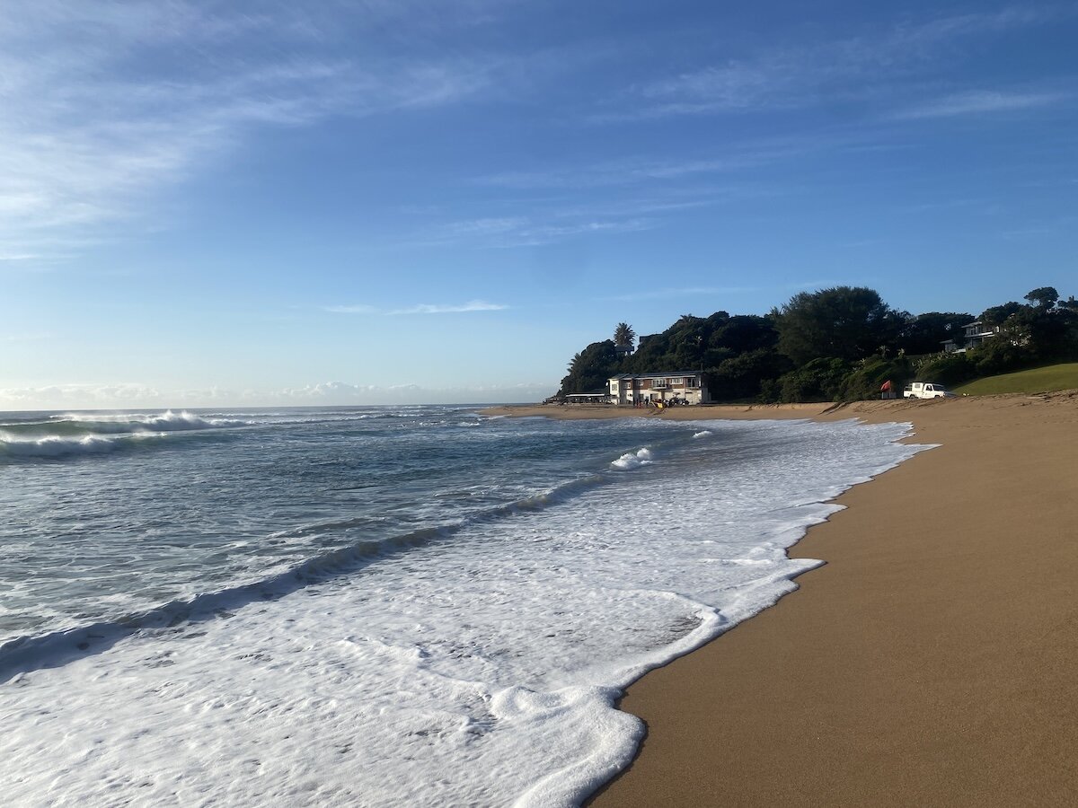 Gentle morning surf washing onto Zinkwazi main beach with the ski boat club in the distance