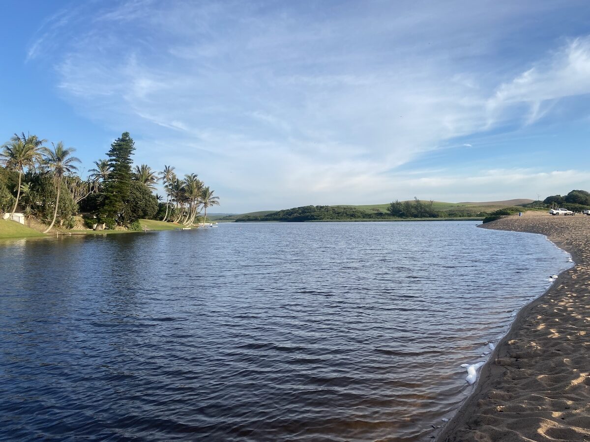 Calm Zinkwazi lagoon at sunrise with palm trees and rolling green hills