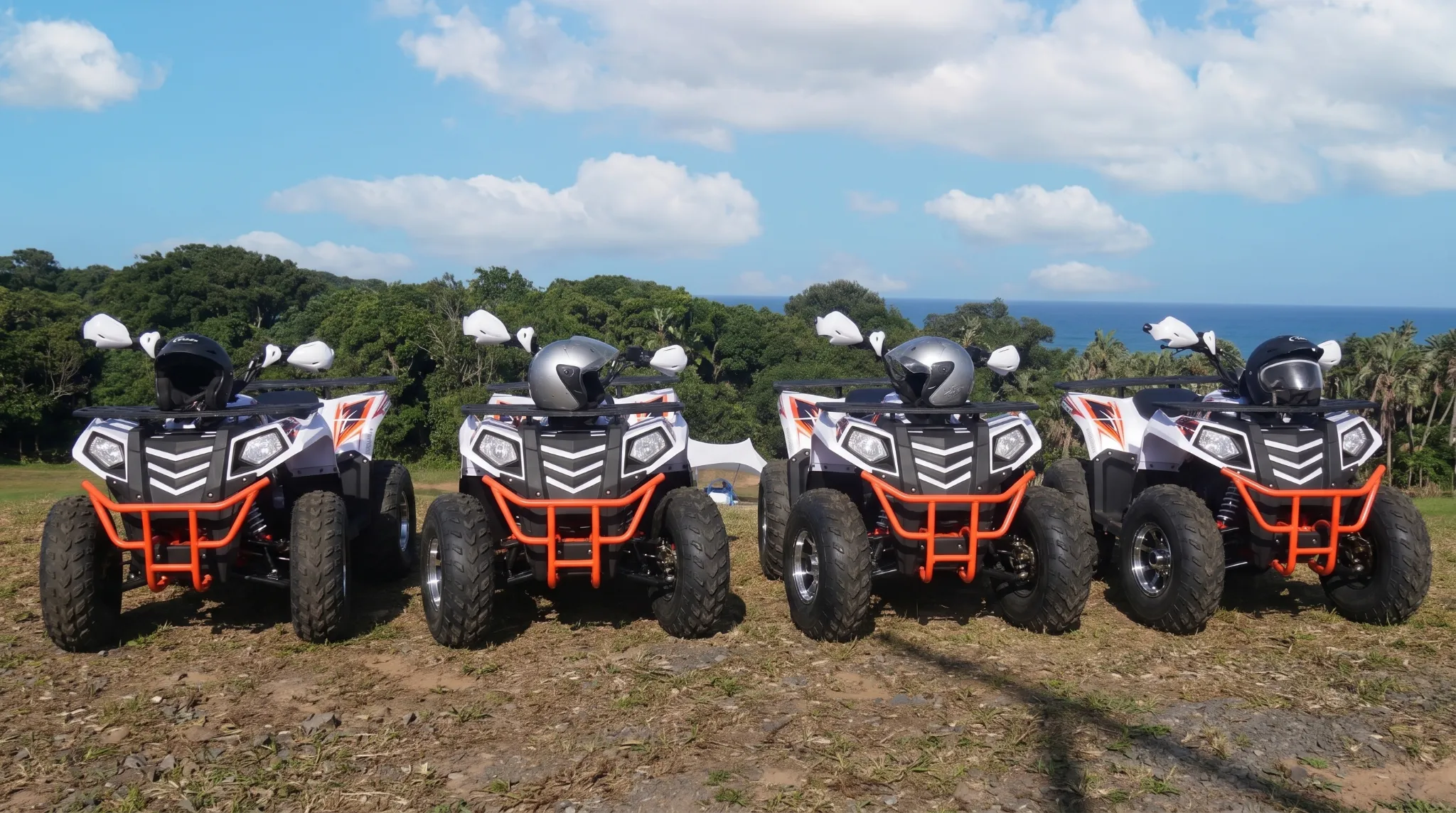 Four quad bikes with helmets parked on a dirt path with trees and the ocean, for adventures near Ballito.