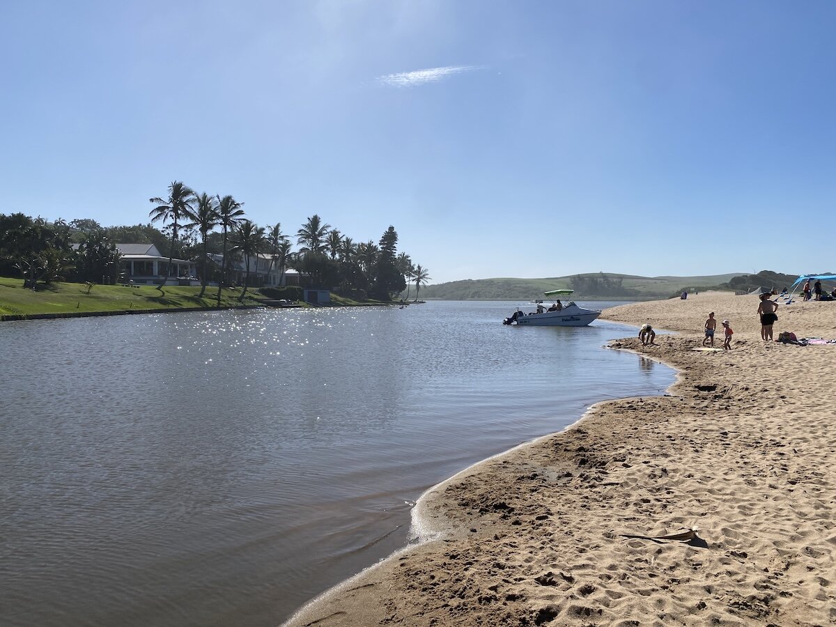 Boat at the mouth of Zinkwazi Lagoon with families playing on the sandy beach