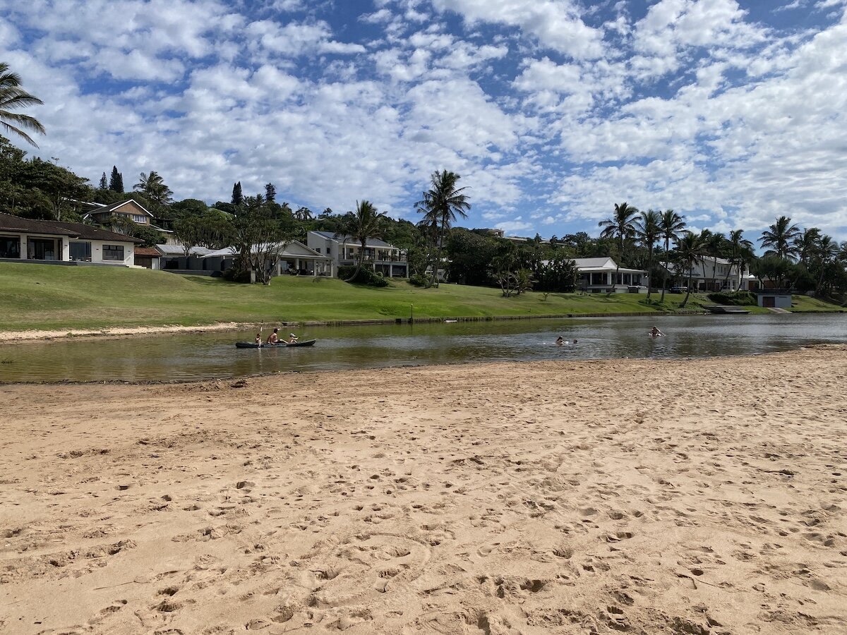 Kayaking and swimming water activities on Zinkwazi Lagoon with palm-lined homes