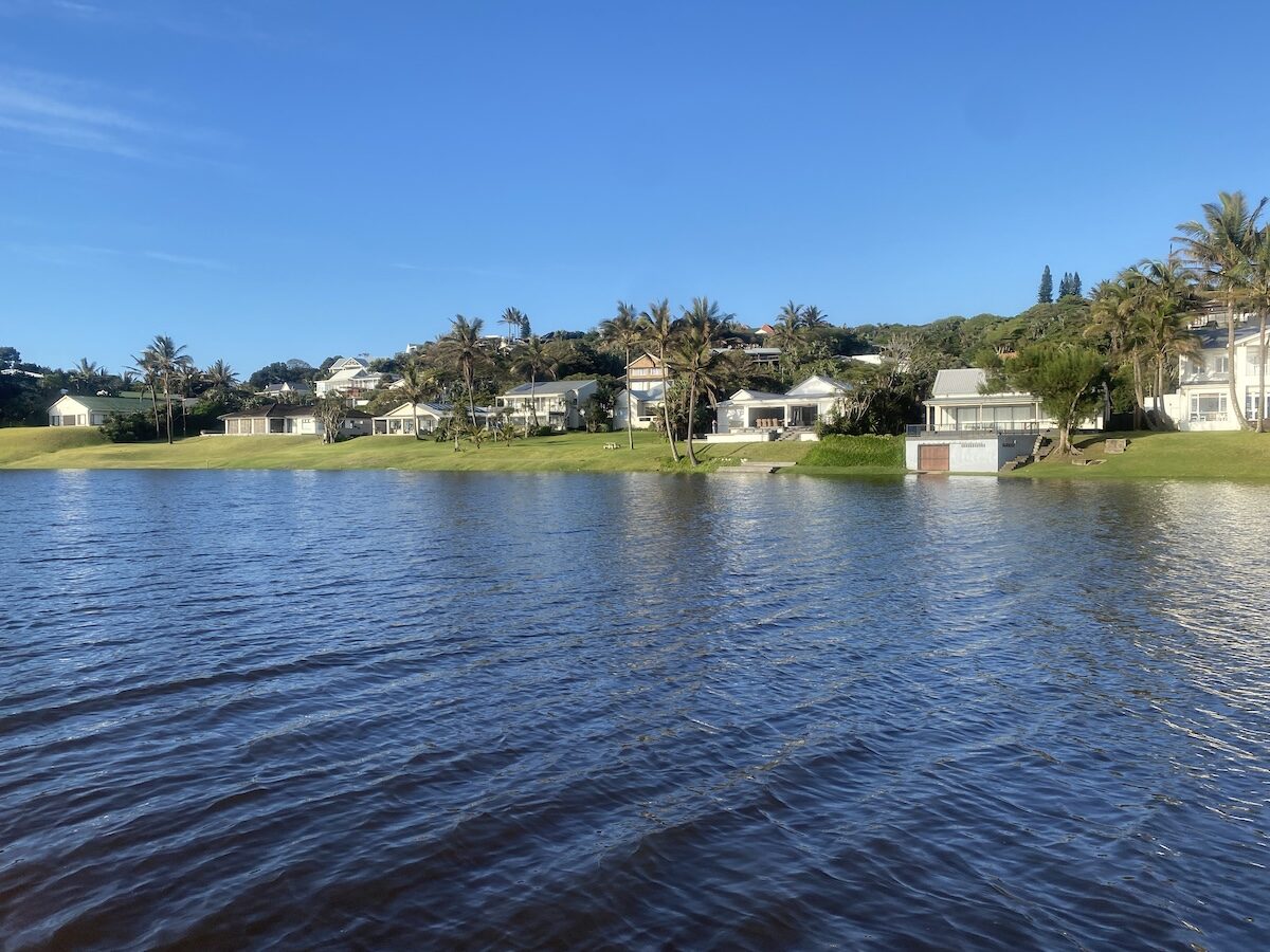Lagoon with waterfront houses and palm trees lining the shore in Zinkwazi under a clear blue sky.