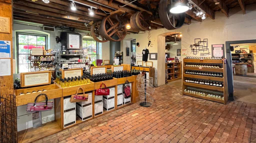 A historic building with exposed beams and brick floors, displaying bottles on shelves and tables inside Cedarburg.