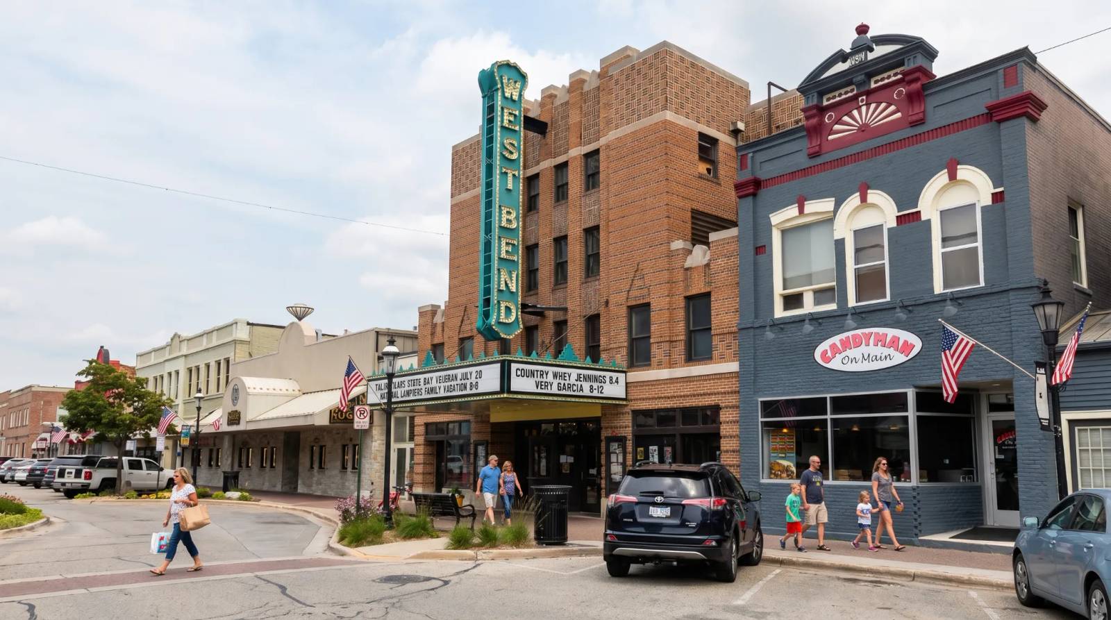 A vibrant street scene at West Bend with historic brick buildings and people strolling the sidewalks on a cloudy day.