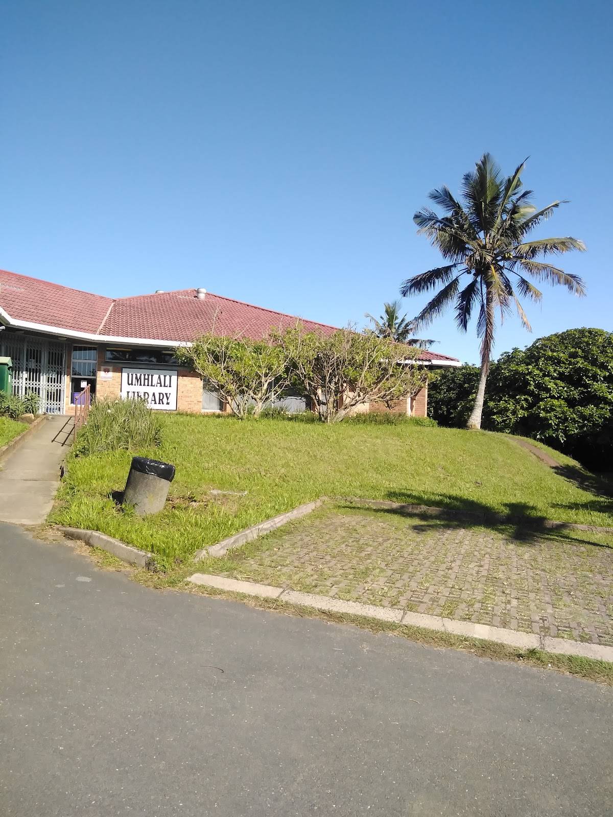 A building with a red tile roof and a palm tree stands on a sunny hillside in Umhlali.