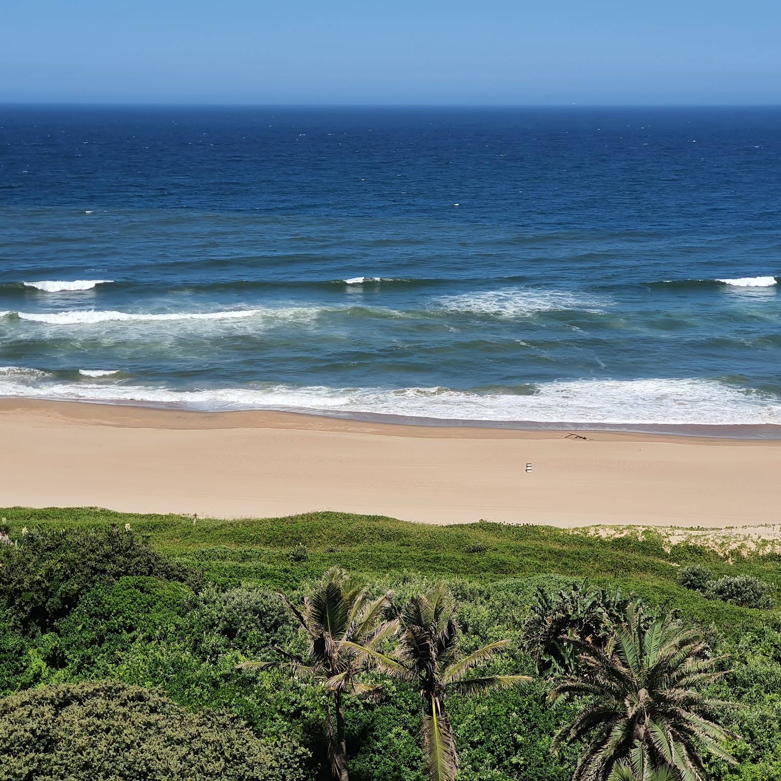 Ocean waves hit a pristine sandy beach framed by lush green vegetation and palm trees in Ballito.