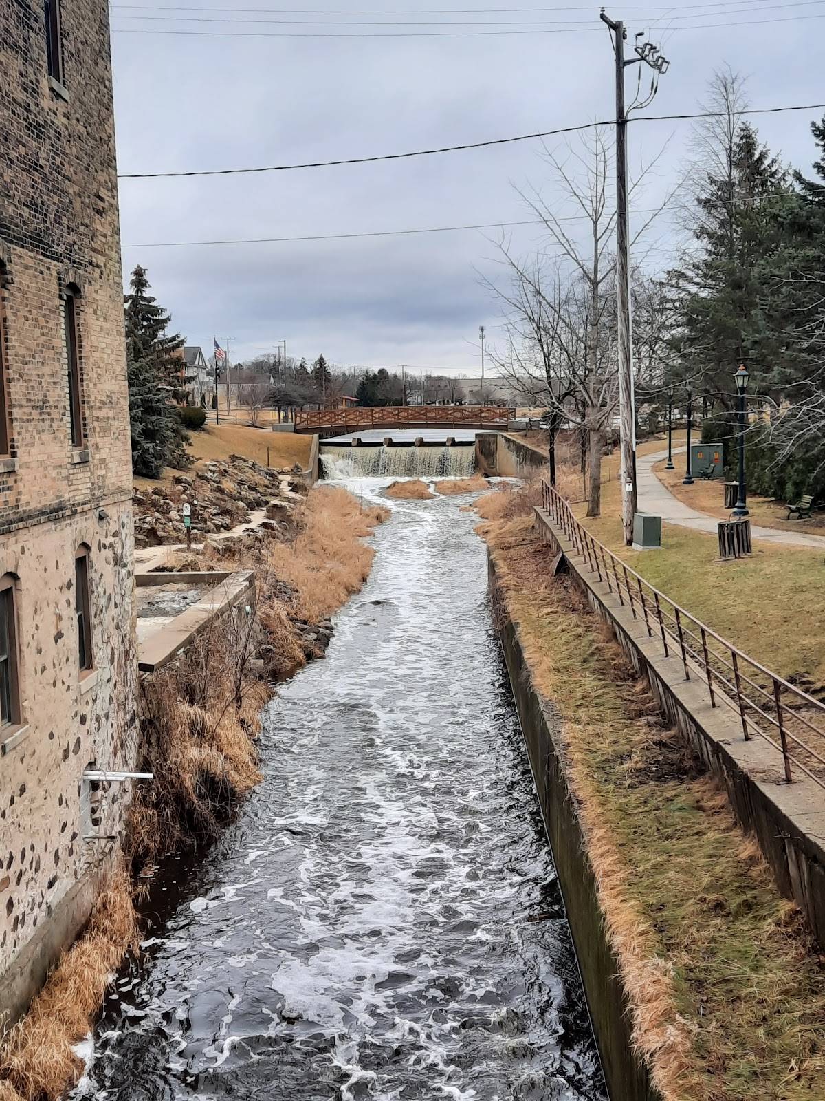 A river with a small dam and bridge, reflecting a cloudy sky above Hartford.
