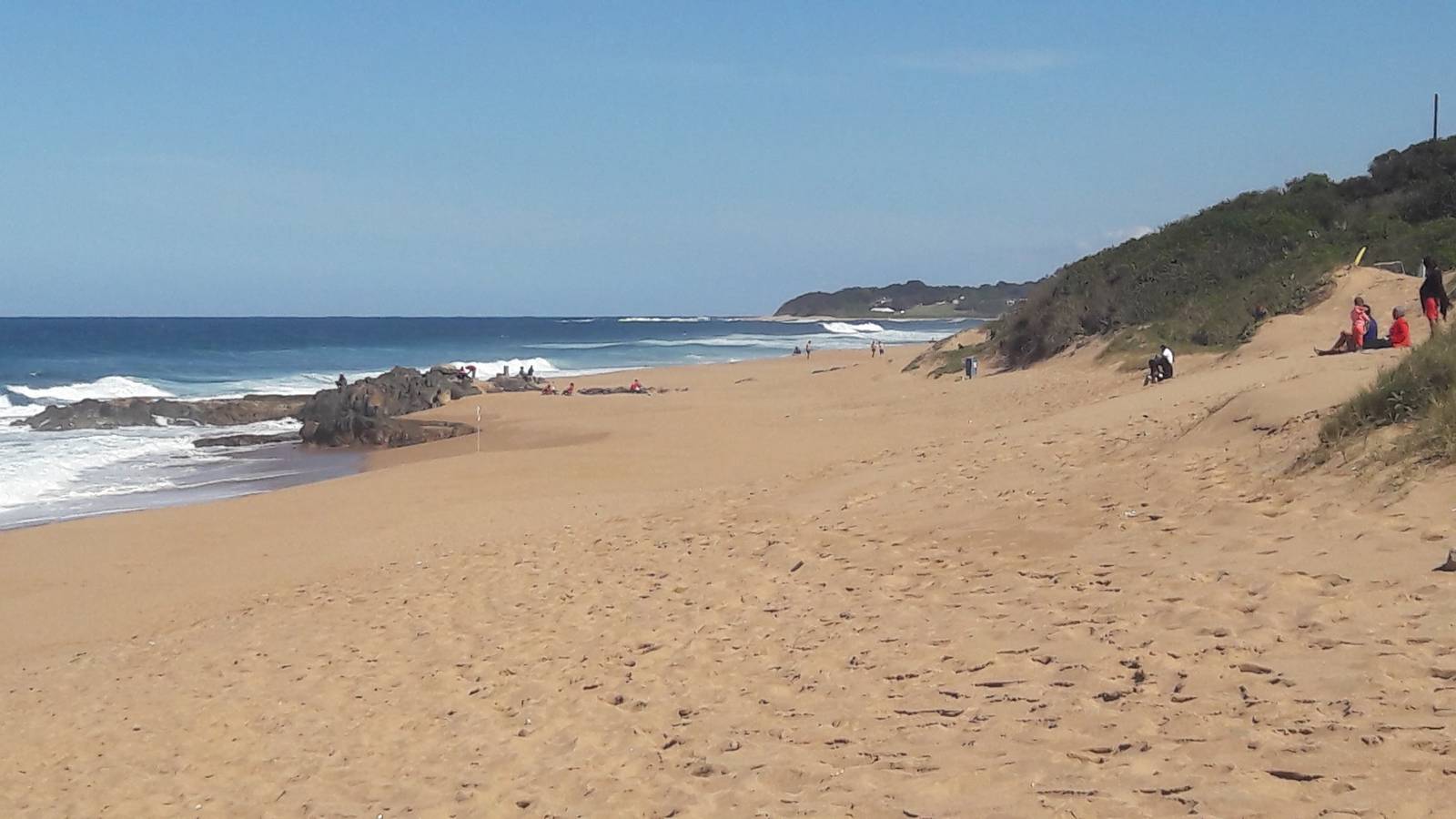 Expansive sandy beach with ocean waves meeting the shore and green hills in the distance at Blythedale.