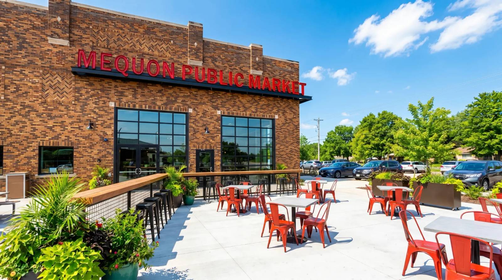 Outdoor patio with orange chairs and tables in front of a brick building at Mequon Public Market.