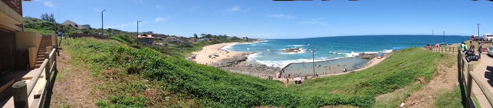 Panoramic view of the beach, coastline, and tidal pool filled with people at Tinley Manor.