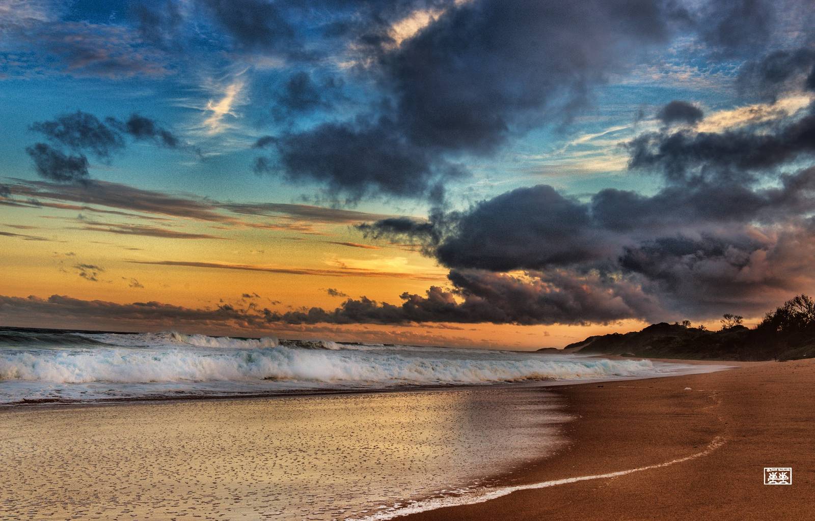 Waves break on Zinkwazi beach at sunset, with golden skies, dark clouds, and a distant treeline.